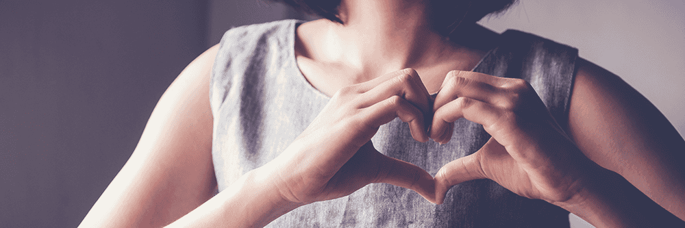 Heart-shaped hands at woman's chest, symbolizing community and kindness, supporting Timebank Ireland initiatives and volunteering efforts.